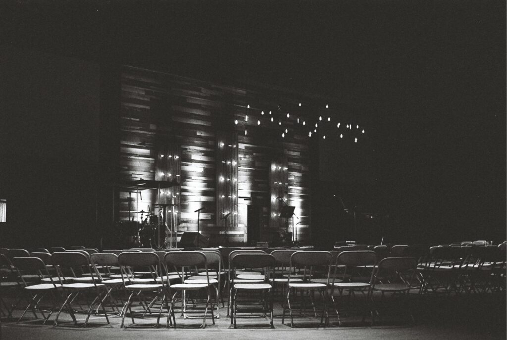 Black and white photo of an empty auditorium with a stage and dramatic lighting, ideal for events.