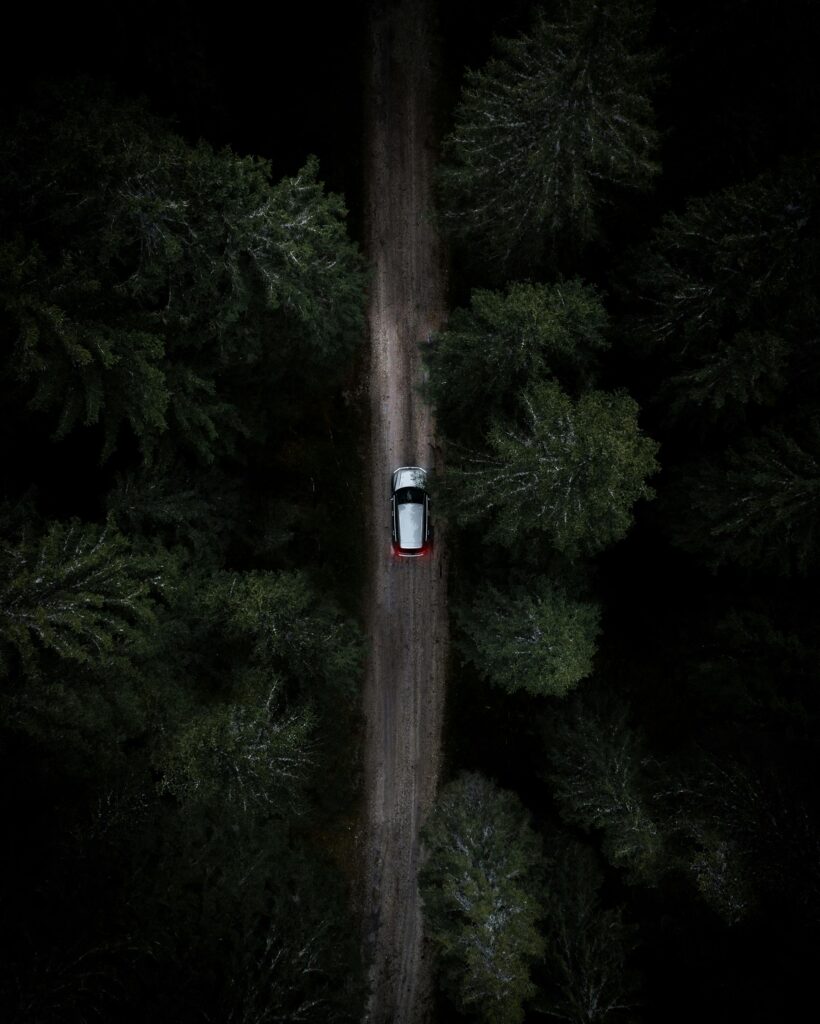 A lone car travels through a dense, dark forest. Aerial view capturing the mood of a secluded road journey.