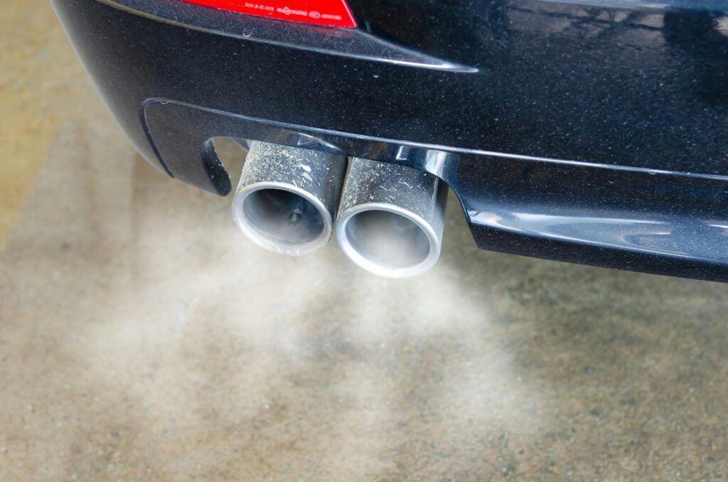 Close-up of a car's exhaust pipes emitting visible smoke, highlighting air pollution.